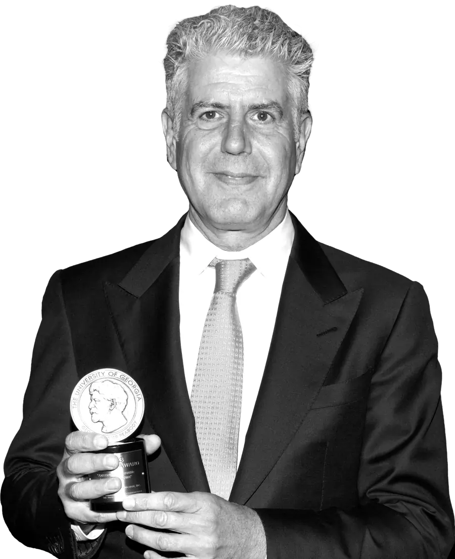 Anthony Bourdain in a dark suit, holding a Peabody Award